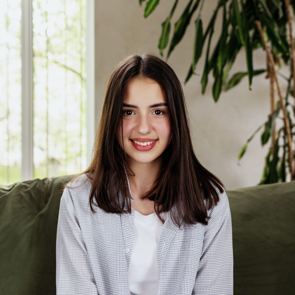 beautiful smiling caucasian girl sitting at green sofa and watching at camera