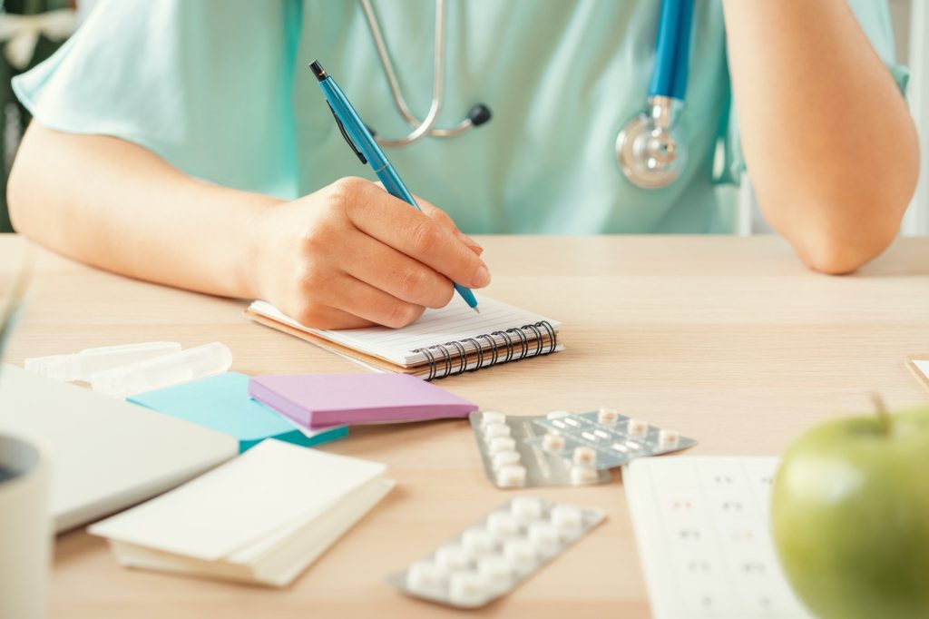 female medicine doctor filling patient medical form or prescription